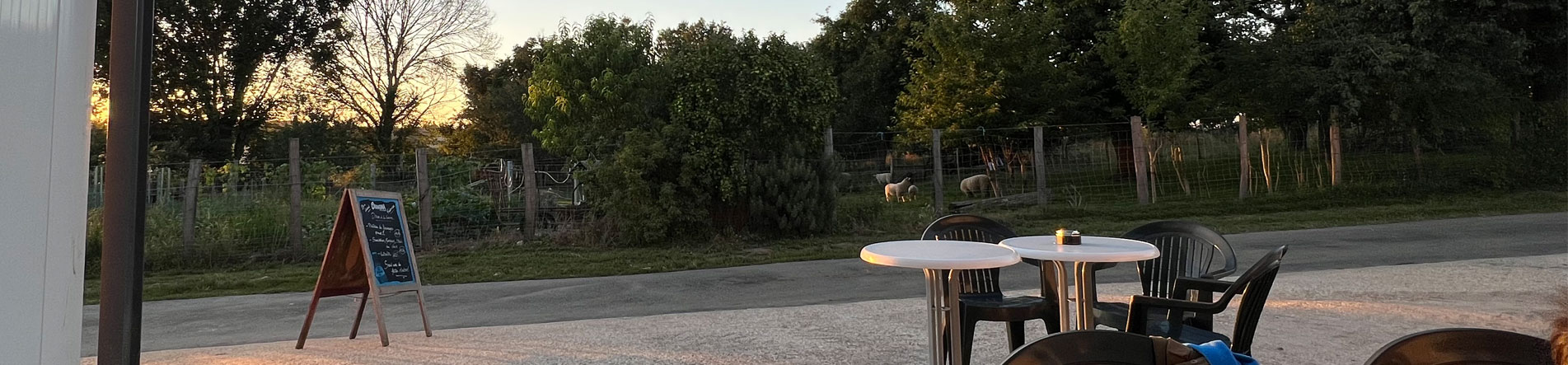 La terrasse de la ferme Lait Meuh au crépuscule : tables et ardoise face au pré